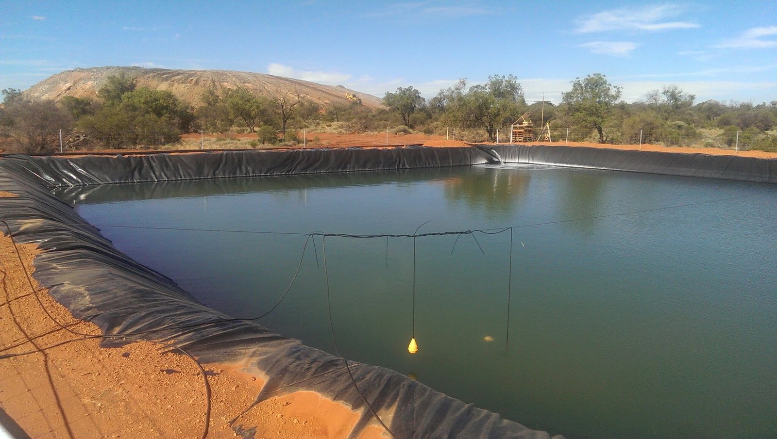 HDPE lined turkey's nest water storage pond with mine rehabilitation works in background